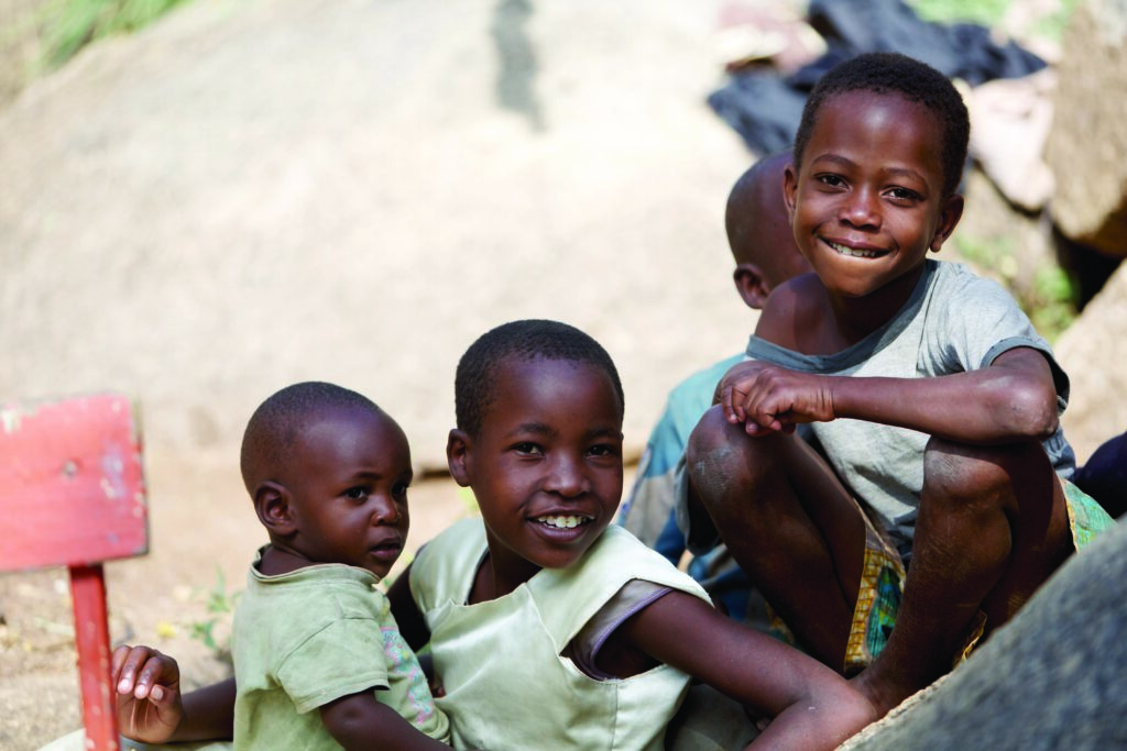 Four kids sitting down outdoors, two smiling at the camera